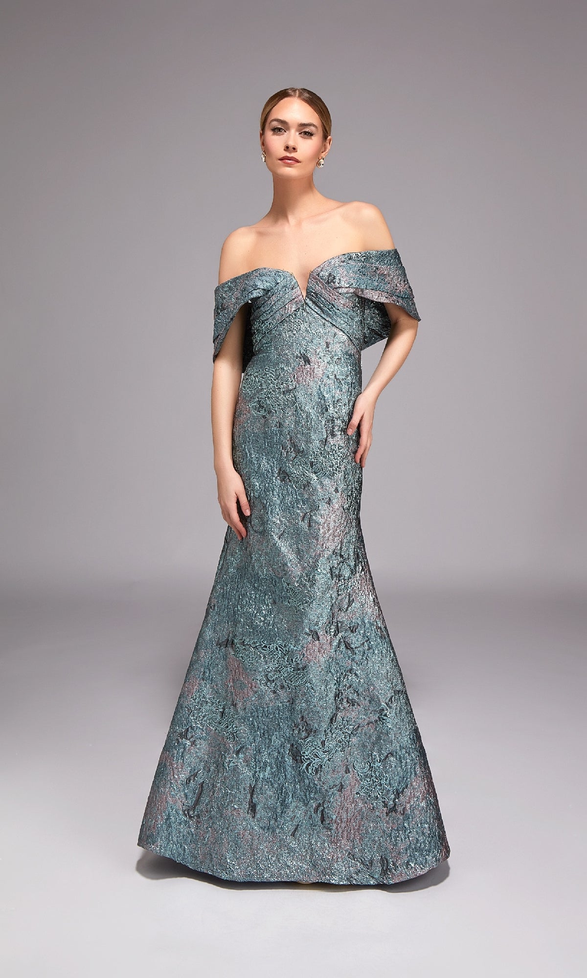 A woman models the Alyce 27794 long formal dress, an off-the-shoulder, floor-length jacquard gown in textured blue, set against a plain grey background—ideal for special events.